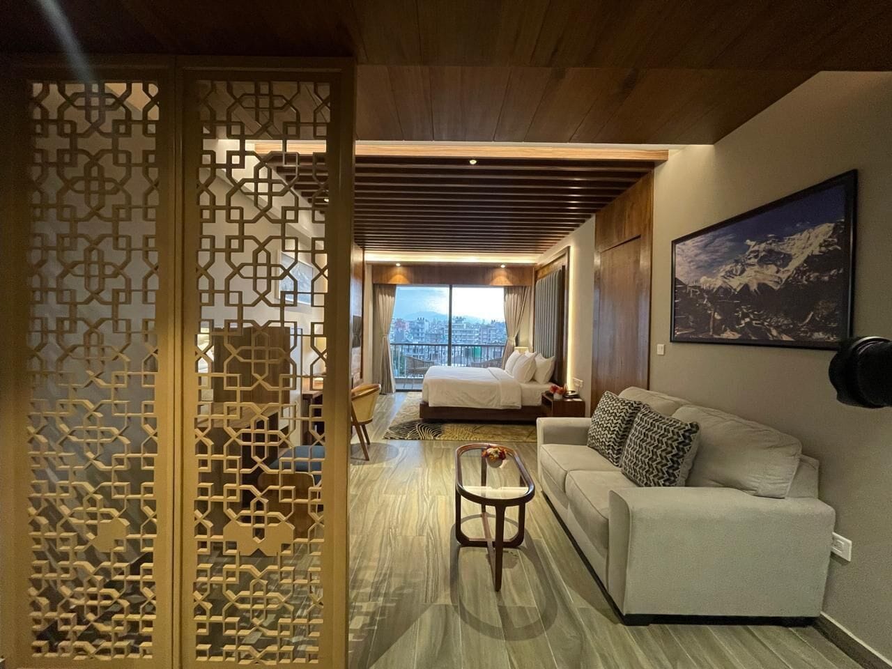 A hotel room with a bed, a sofa, a coffee table, and a decorative screen.