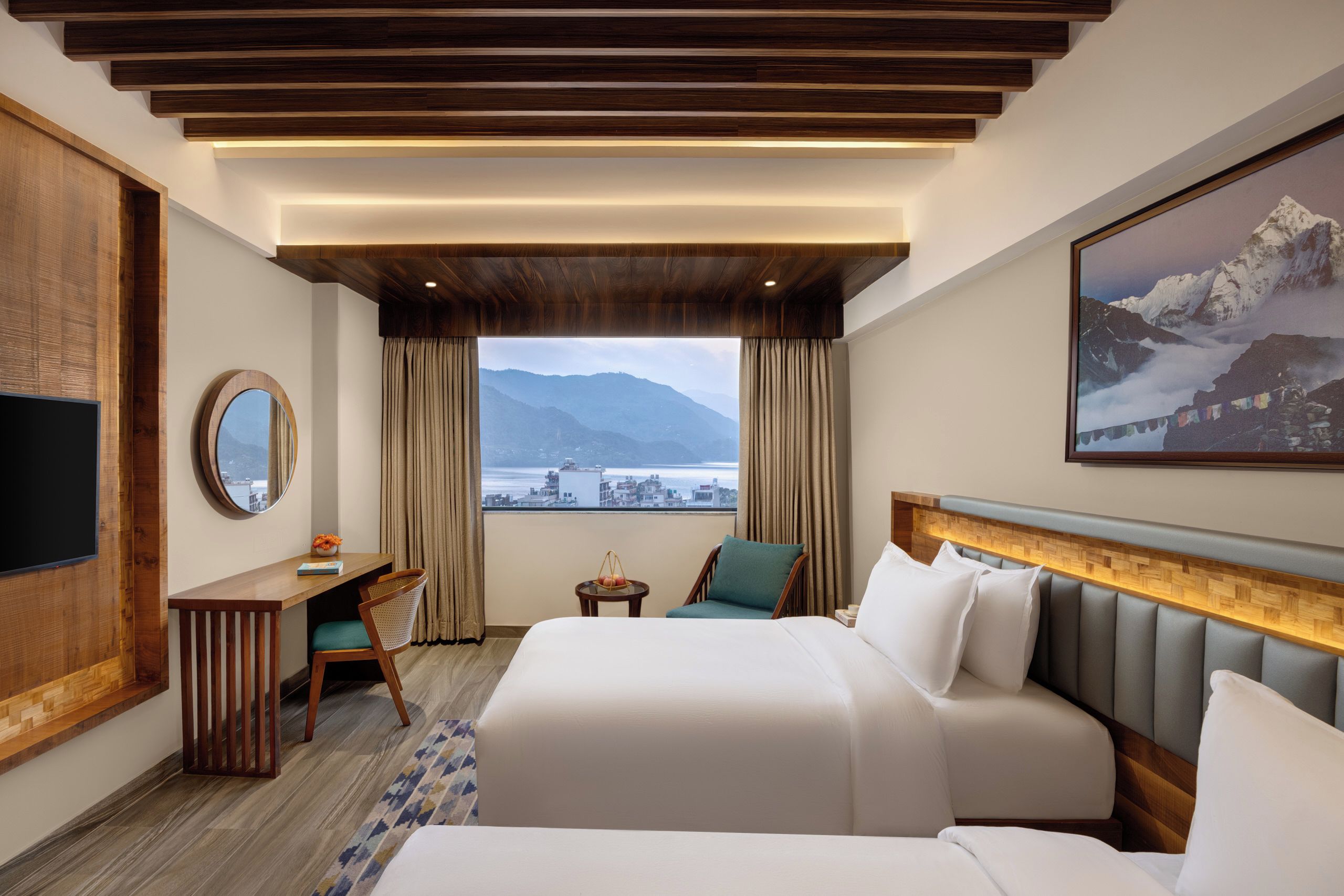 A hotel room with a bed, a desk, a chair, a TV, and a large window with a mountain view.