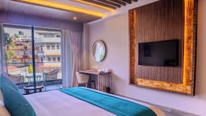 A hotel room with a large bed, a desk with a chair, a TV mounted on the wall, and a balcony with wicker furniture. - Soaltee Westend Lakeside Pokhara (Pokhara)