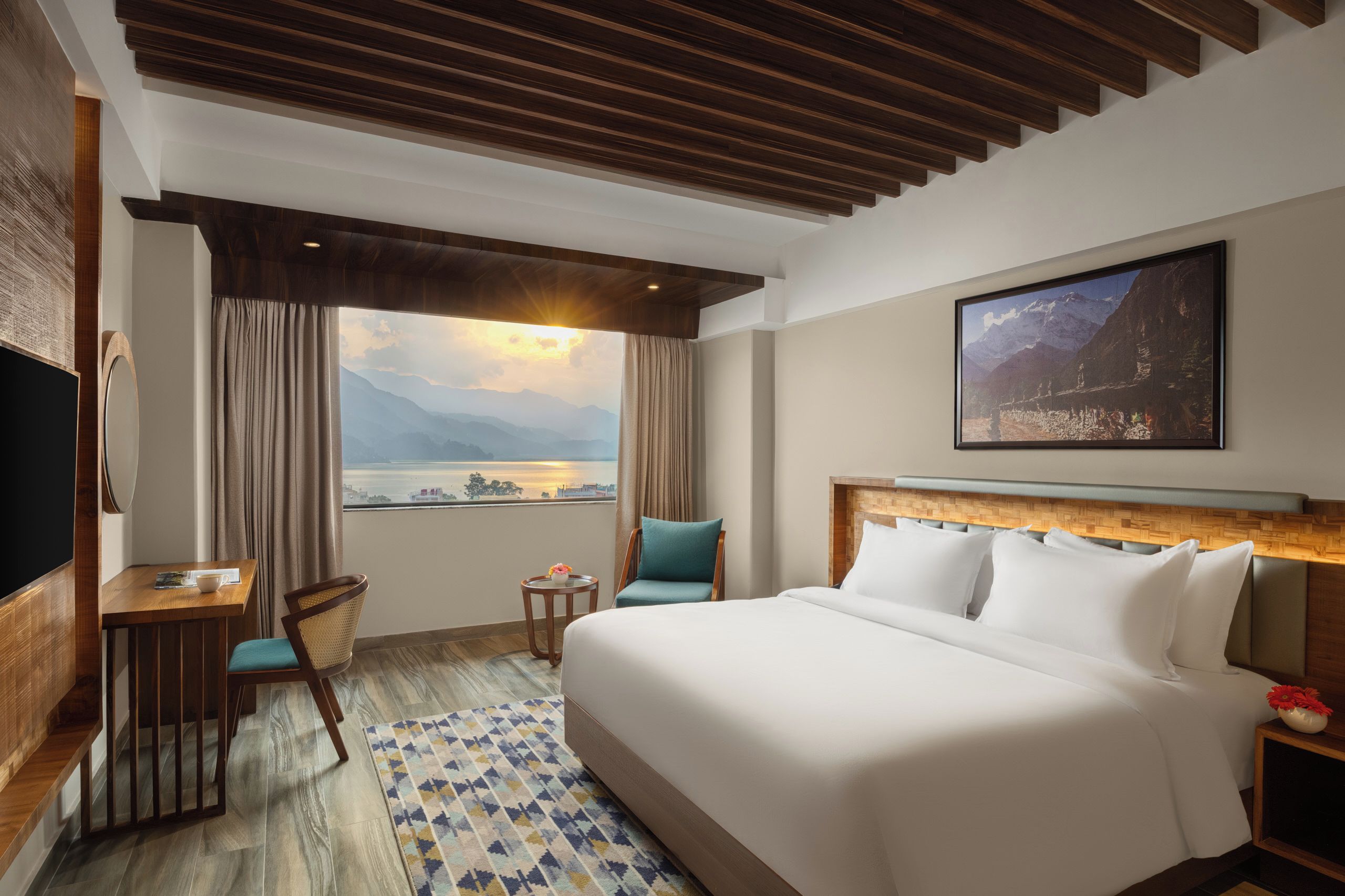 Habitación de hotel con cama, escritorio, silla, vista a las montañas y un cuadro en la pared.