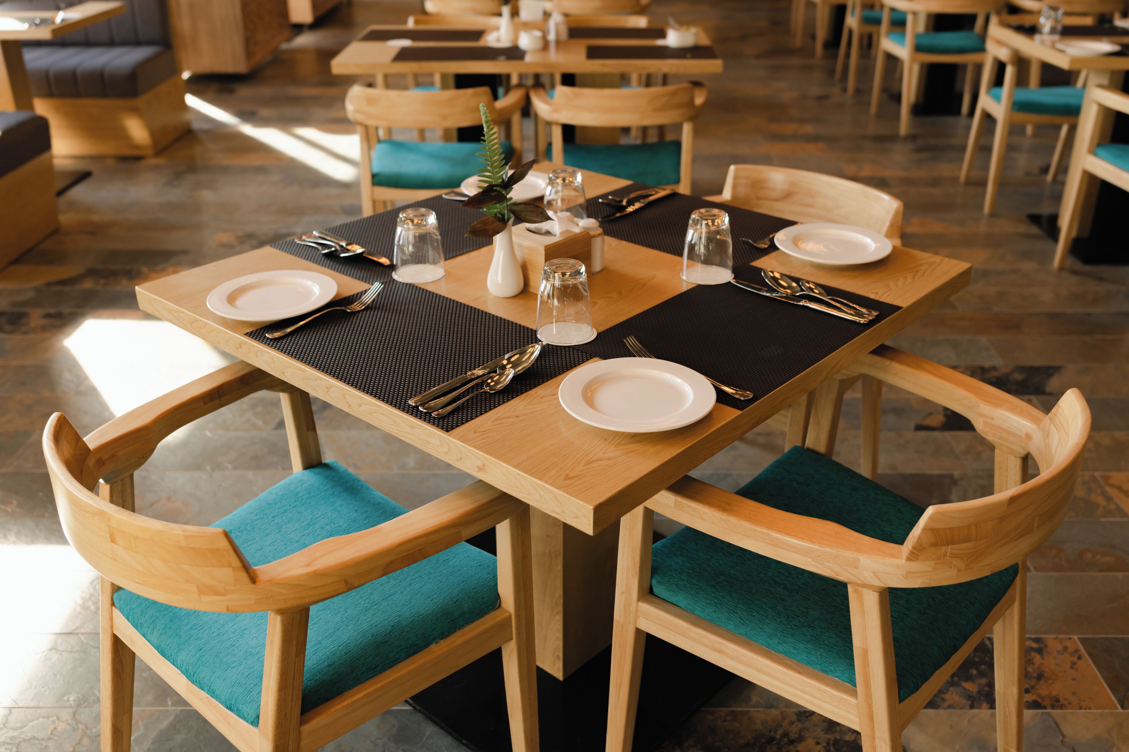 Un comedor con mesas y sillas de madera, cada juego con platos, cubiertos y saleros y pimenteros.