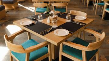Un comedor con mesas y sillas de madera, cada juego con platos, cubiertos y saleros y pimenteros.