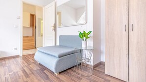 Une pièce avec un canapé gris, une petite table sur laquelle est posée une plante, un miroir et une armoire.