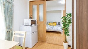 A compact room with a bed, a microwave, a refrigerator, a chair, and a potted plant. - 2/6/MAX4/Nakanoshinbashi (Tokyo)