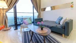 A modern living room with a sofa, a coffee table, a lamp, and a view through large windows. - Cozy & Luxury Apartments, 5mins to Legoland (Iskandar Puteri)