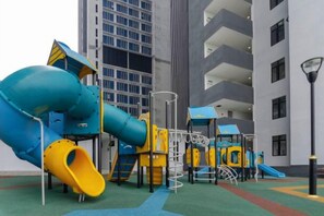 A playground with slides and climbing structures, set against a building with balconies. - Cozy & Luxury Apartments, 5mins to Legoland (Iskandar Puteri)