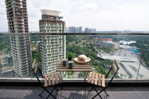 A balcony with a table and chairs, overlooking a cityscape with high-rise buildings and greenery. - Cozy & Luxury Apartments, 5mins to Legoland (Iskandar Puteri)