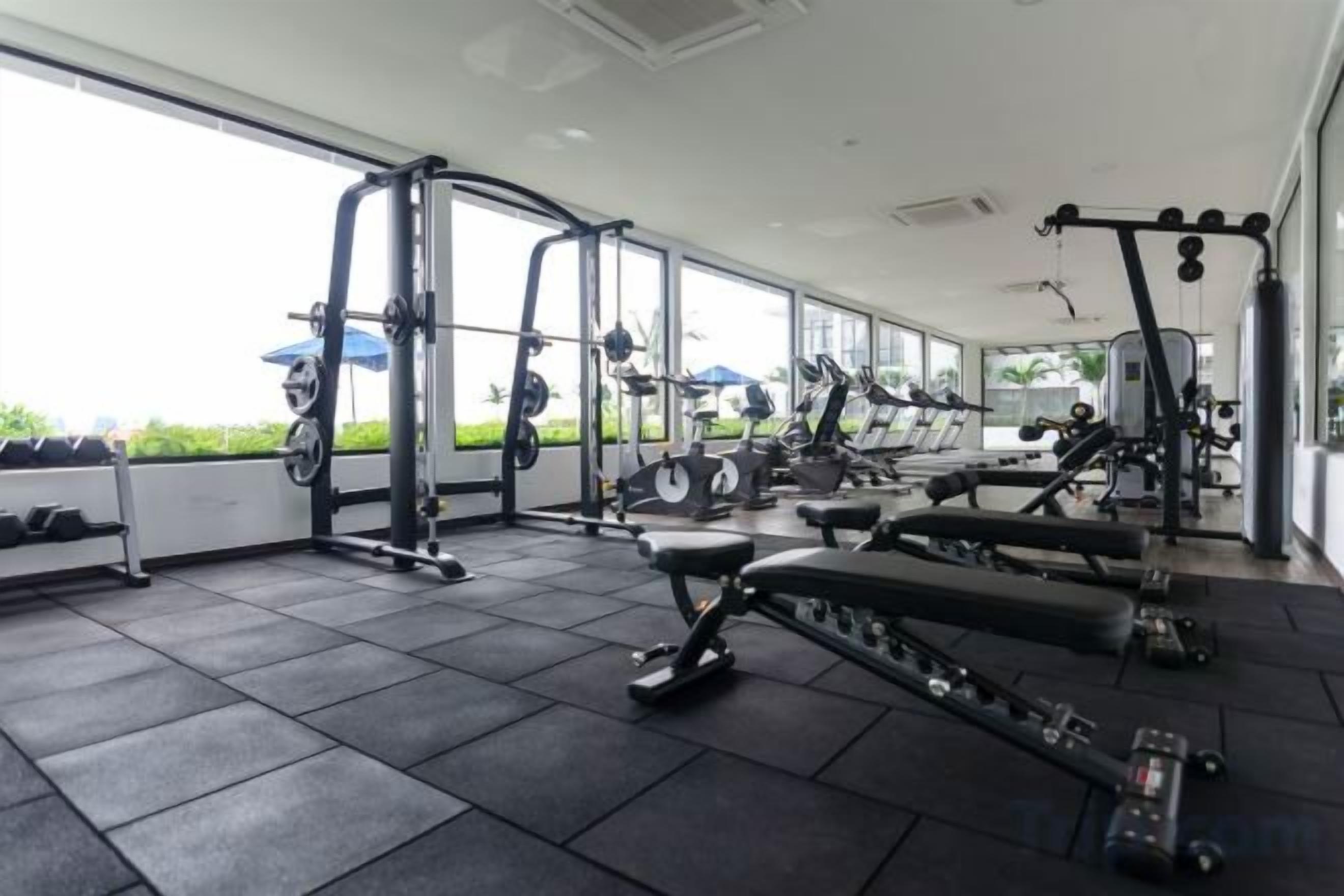 A gym with various exercise equipment, large windows, and a view of greenery outside.