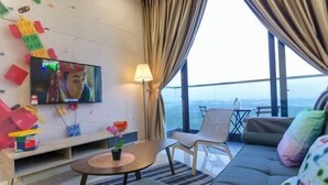 A modern living room with a television, a sofa, a small table with a plant, and a view of the city. - Cozy & Luxury Apartments, 5mins to Legoland (Iskandar Puteri)