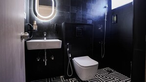 Uma casa de banho moderna com uma pia branca, um espelho iluminado, sanita e chuveiro.