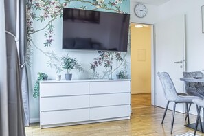 Un salon moderne doté d’un téléviseur à écran plat, d’un meuble blanc et d’un coin repas avec une table et des chaises.