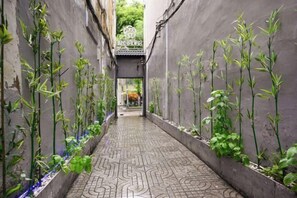 A narrow alley with patterned paving, flanked by vertical plantings and a metal gate at the end. - Ben Thanh Inn - M&A (Ho Chi Minh City)