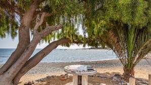 Uma mesa à beira-mar com tampo de mosaico, rodeada por pedras e uma árvore.