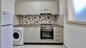 Een koelkast, een oven, een kookplaat, kookgerei, borden en bestek