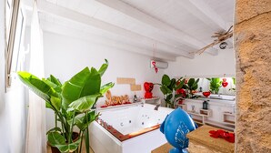 Une pièce avec une baignoire blanche, des plantes en pot, une chaise bleue et un mur en pierre.