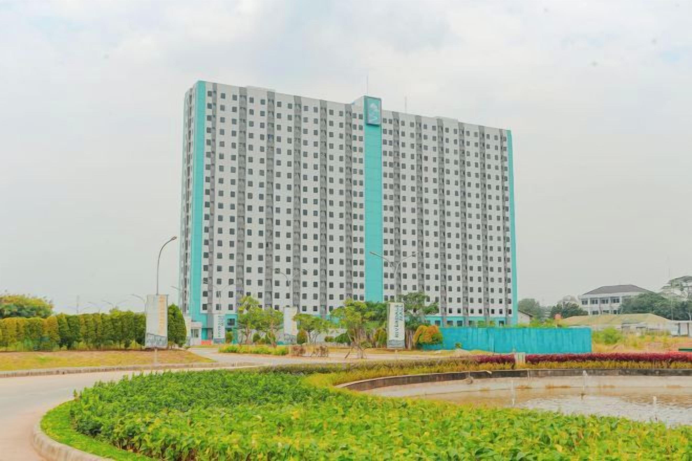 A high-rise building with a uniform facade, surrounded by a landscaped area with a circular garden and a small pond.