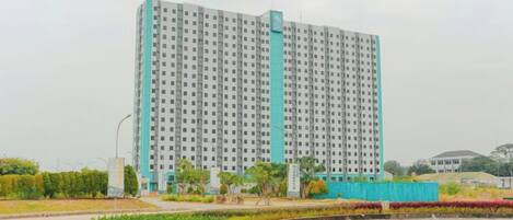A high-rise building with a uniform facade, surrounded by a landscaped area with a circular garden and a small pond.