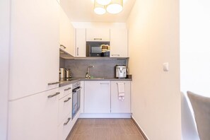 A compact kitchen with white cabinets, a microwave, a coffee maker, and a small countertop.
