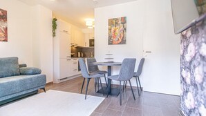 Ett modernt vardagsrum med en soffa, ett matbord med stolar, ett kök i bakgrunden och konstverk på väggarna.