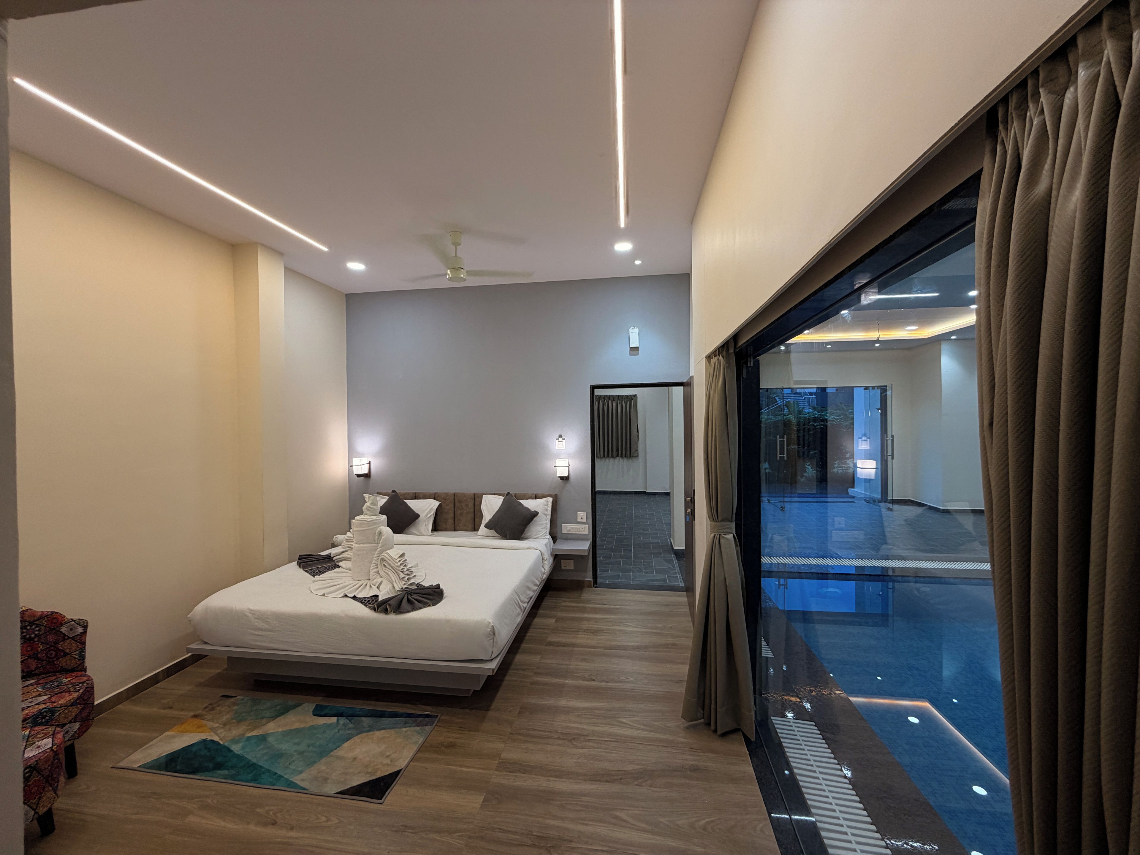A modern hotel room with a large bed, a view of a swimming pool, and a glass door leading to a balcony.