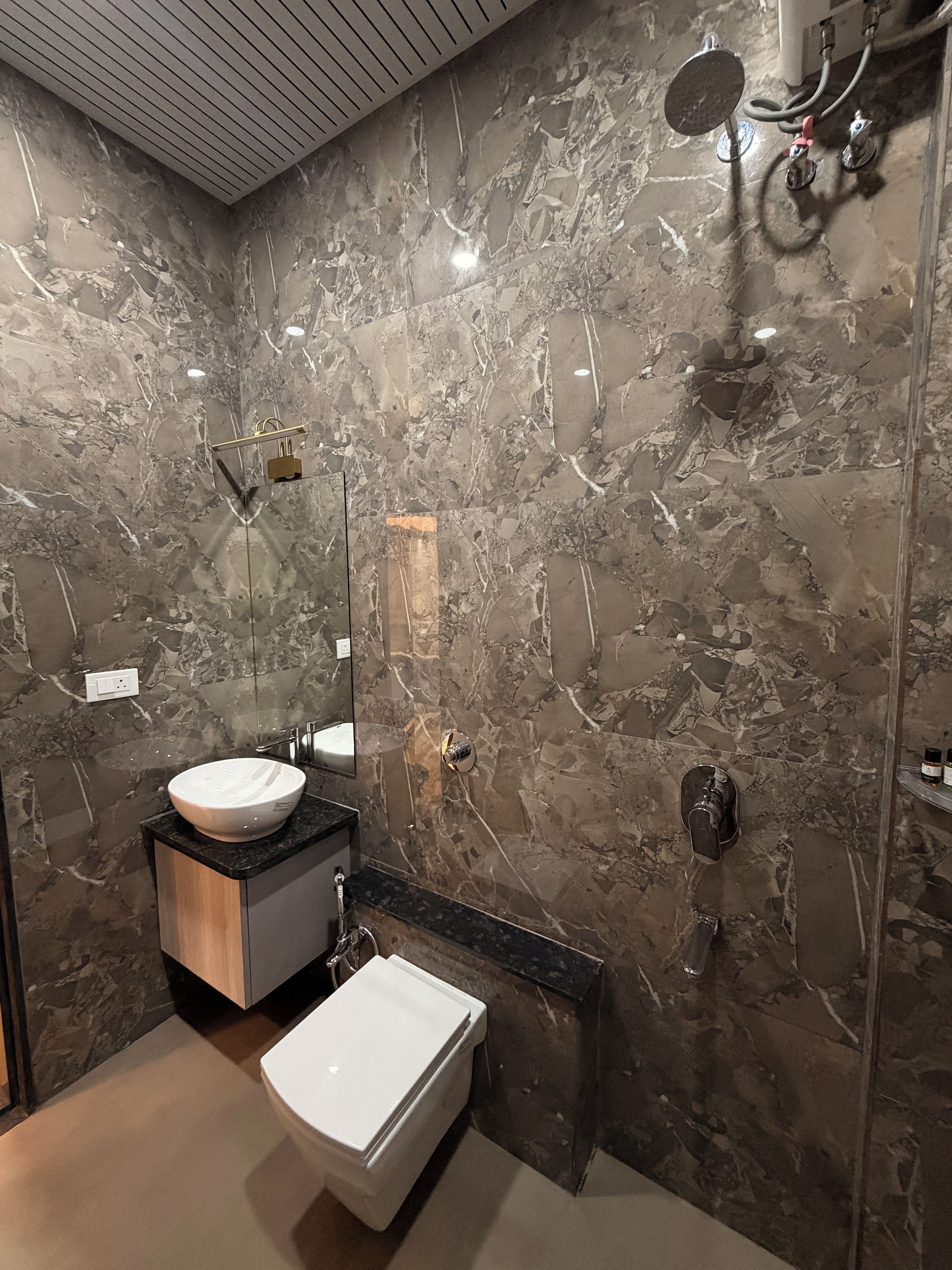 A modern bathroom with a marble wall, a sink, a bidet, and a shower.
