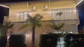 A two-story building with a balcony, air conditioning units, and a well-lit entrance.