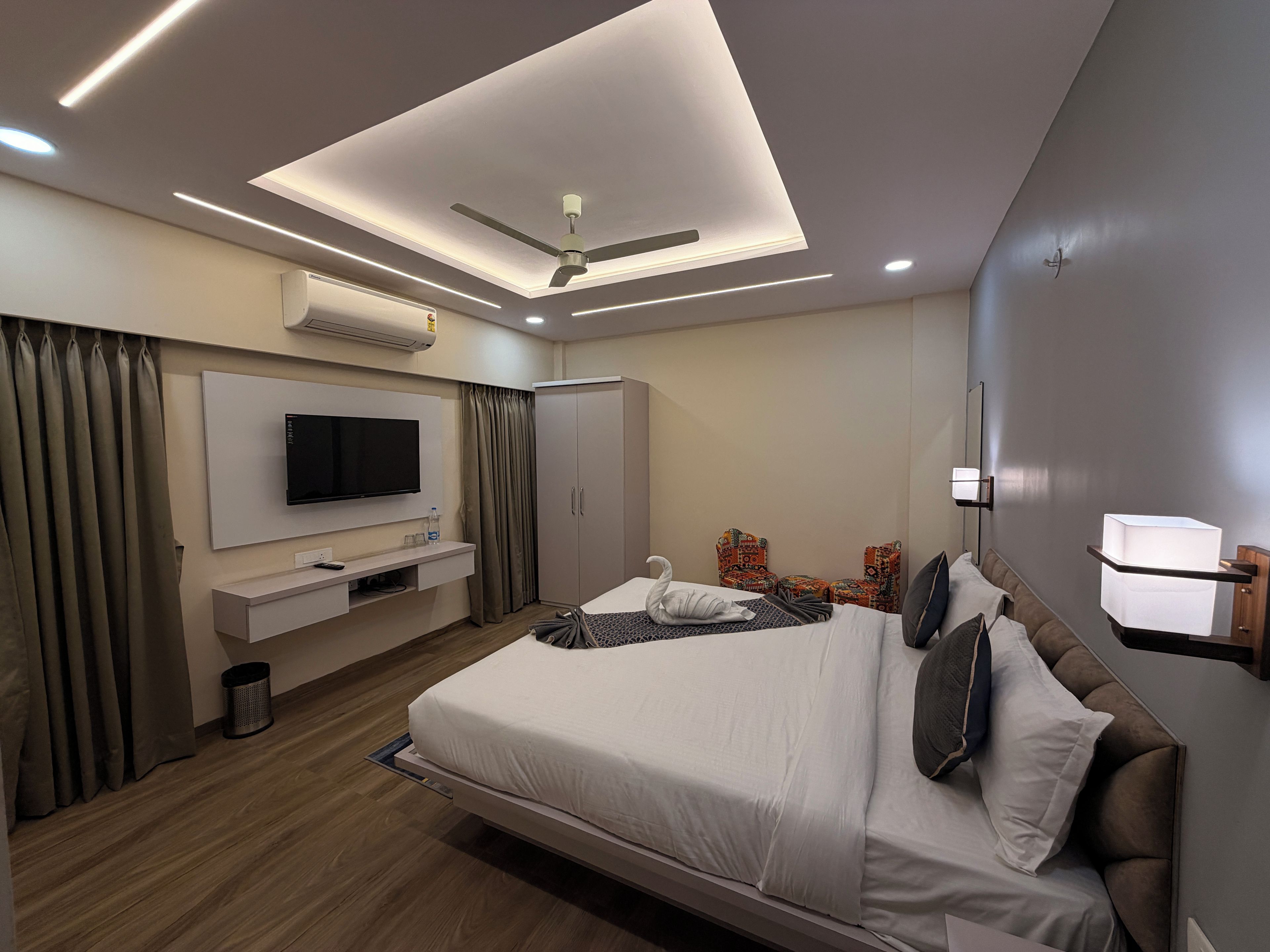 Une chambre d’hôtel moderne équipée d’un lit, d’un téléviseur à écran plat, d’un ventilateur de plafond et d’un mini-bar.