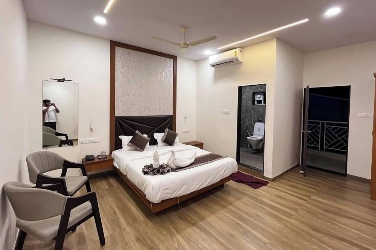 Ein modernes Hotelzimmer mit einem Bett, einem Sessel, einem Spiegel, einer Klimaanlage und einer Tür zu einem Balkon.