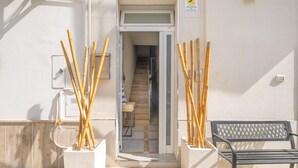 Entrada de un edificio con un banco y cañas de bambú en macetas.