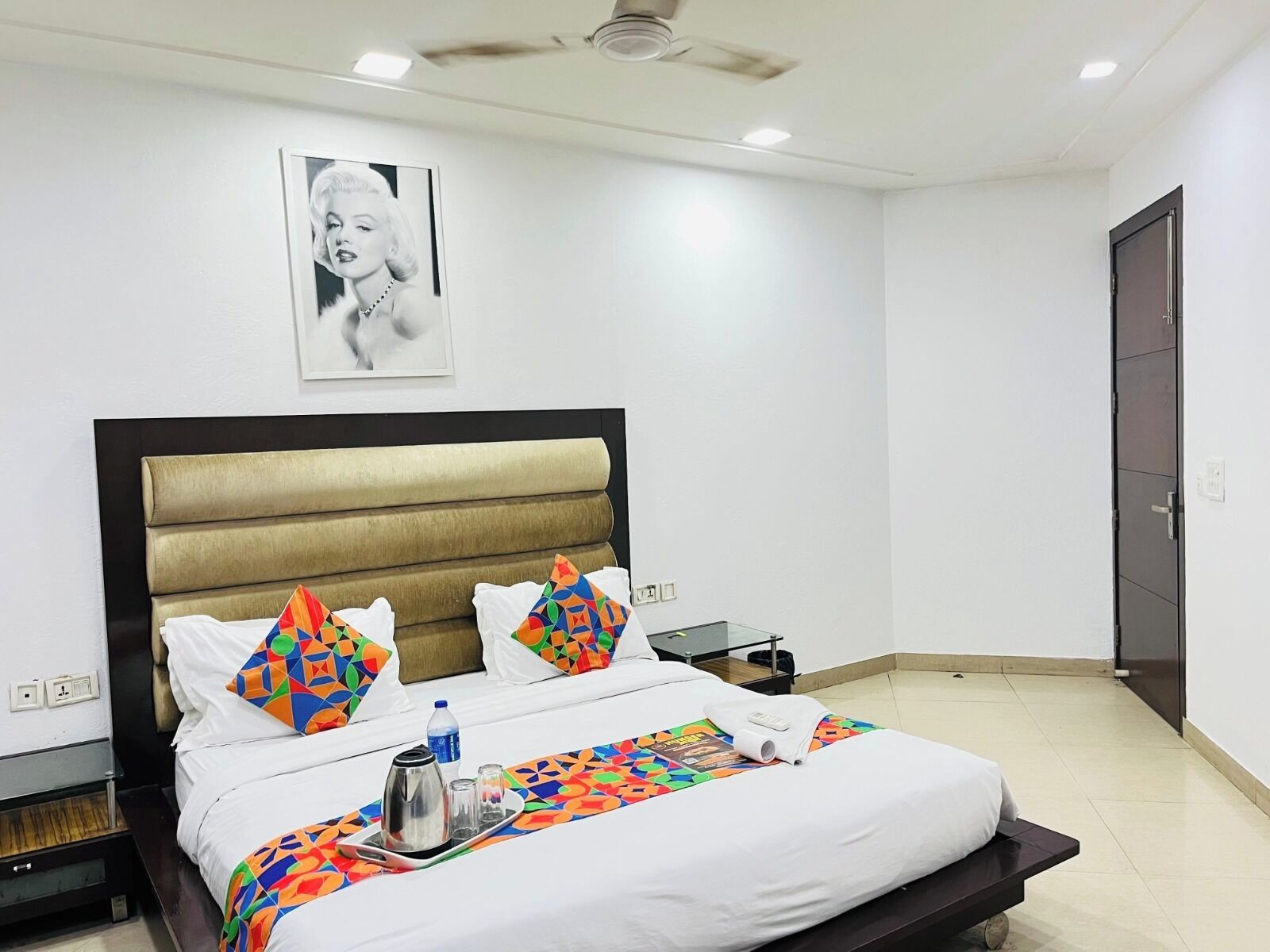 A hotel room with a bed, a bedside table, a nightstand, a ceiling fan, and a door.