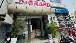 Hotel Le Grand con una entrada destacada, un letrero visible del Banco Bandhan y motocicletas estacionadas afuera.