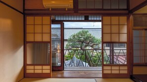 A traditional Japanese room with tatami flooring, sliding doors, and a view of a tree and buildings outside. - Nijo Ohan (Kyoto)