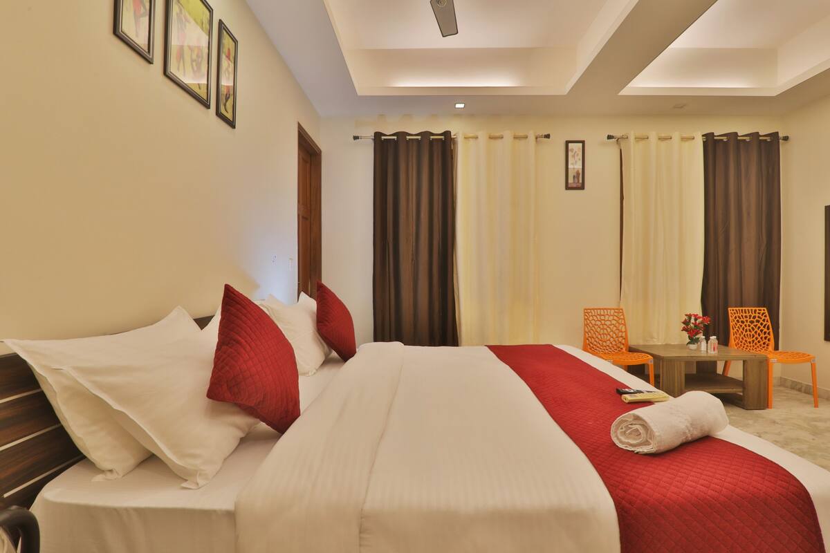 A hotel room with a bed, a desk, two chairs, and a small table with a vase of flowers.