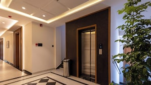 En hotellobby med ett rutmönstrat golv, en hiss, en papperskorg och en krukväxt.