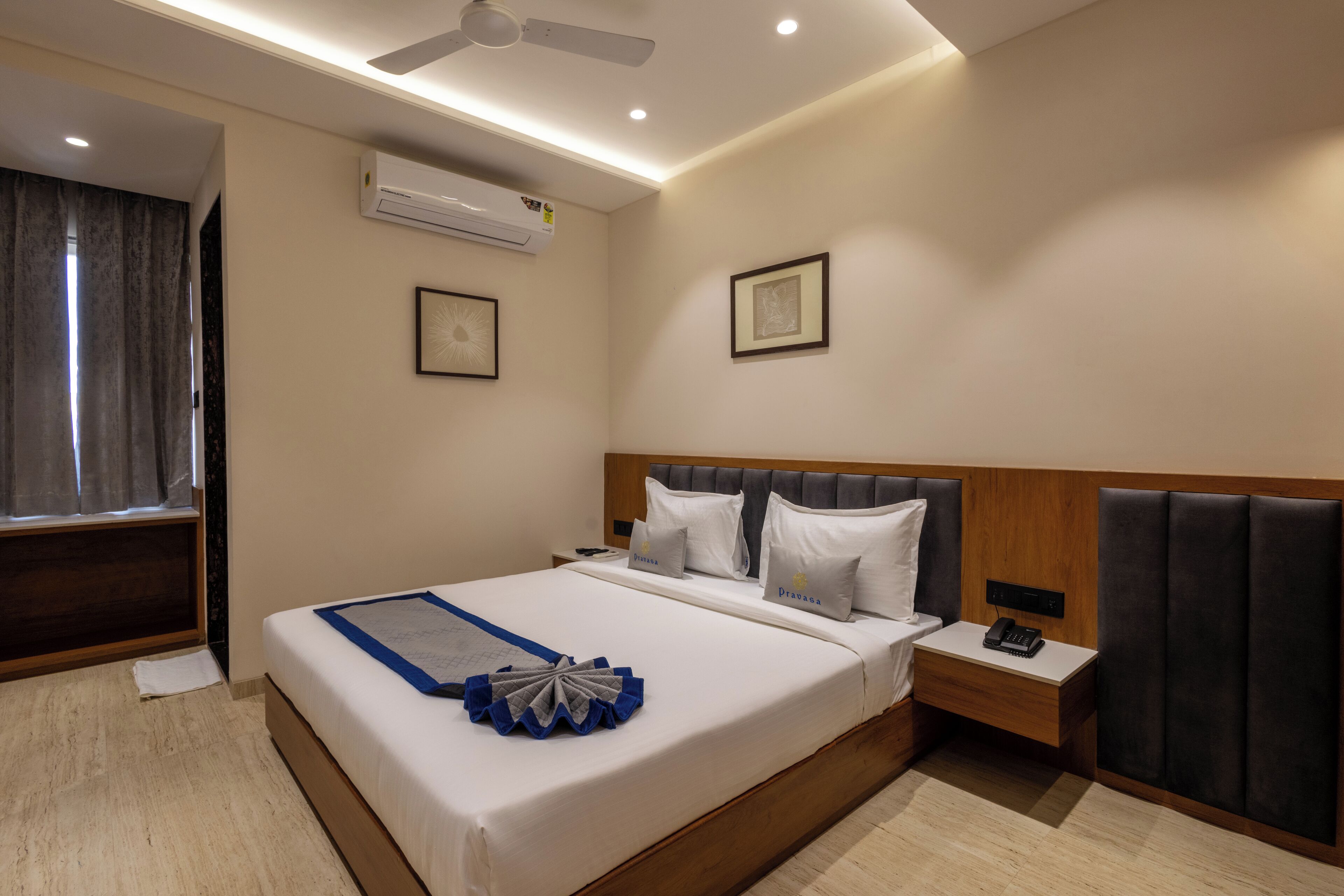 Habitación de hotel con una cama grande, una mesita de noche con teléfono, aire acondicionado de pared y ventilador de techo.