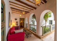 A cozy interior with a red sofa, wooden beams, and arched windows overlooking greenery. - Luxury and super-stylish riad in the heart of Marrakech Médina, fully staffed (Marrakech)