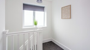 A hallway with a white railing, a window with a blue blind, a hanging light fixture, and a framed artwork on the wall. - 9 Monks Crescent (Durham)