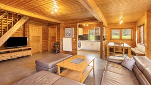 A log cabin interior with a living room, sofa, table, kitchen, and staircase.