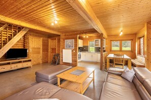 A log cabin interior with a living room, sofa, table, kitchen, and staircase.