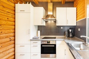 A modern kitchen with white cabinetry, a stainless steel range hood, a built-in oven, and a coffee maker. - Holiday Home 'Blockhaus Marie' with Sauna, Private Terrace and Private Garden (Frielendorf)