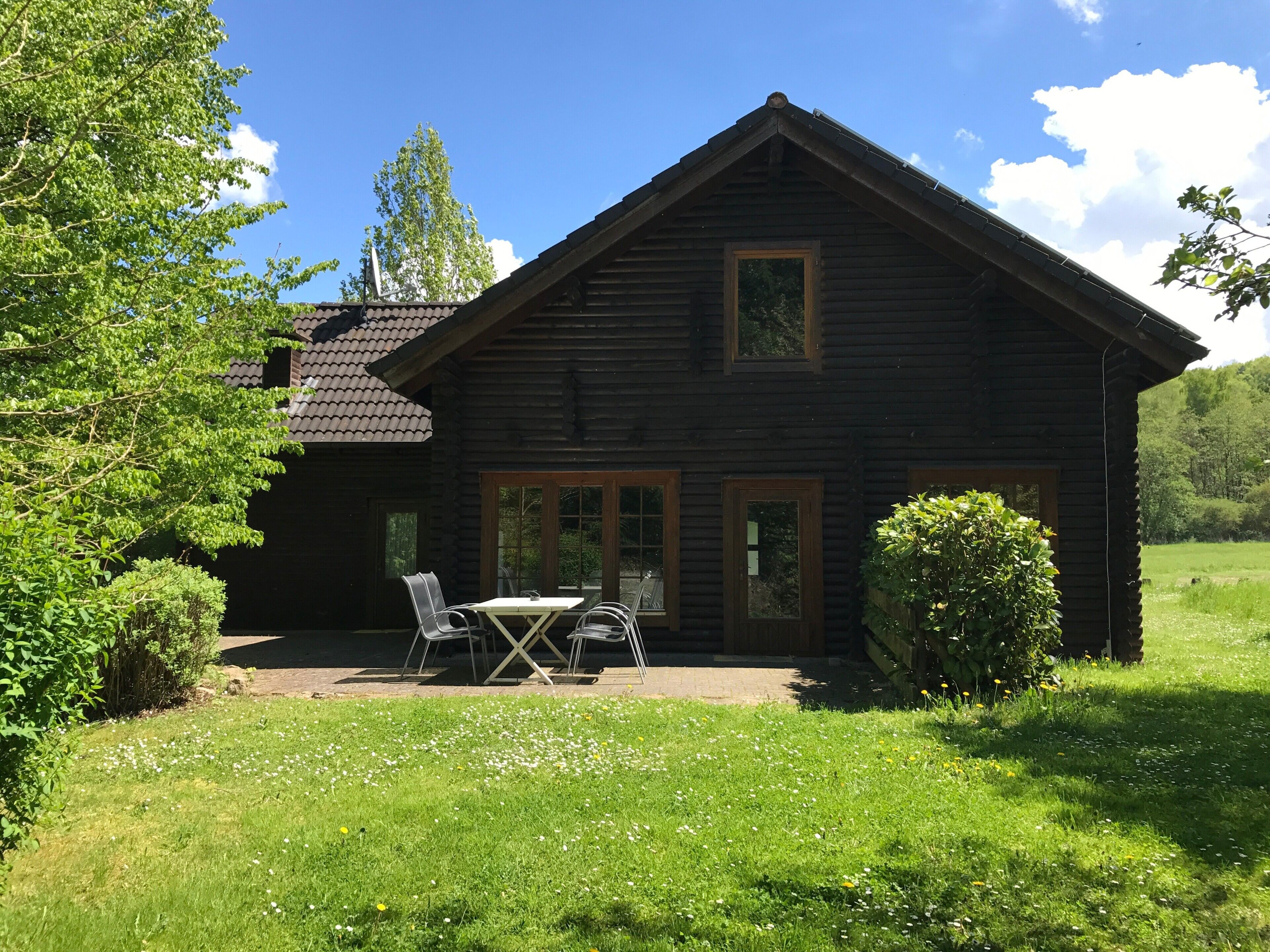 Eine Holzblockhütte mit Terrasse, Tisch und Stühlen.