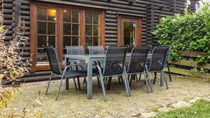 A log cabin with a patio table and chairs, large windows, and a wooden fence.