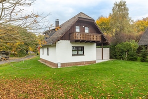 Une maison à deux étages avec un balcon, une cheminée et une pelouse bien entretenue.