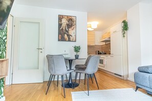 Une cuisine moderne avec des meubles blancs, un coin repas avec deux chaises grises et une petite table agrémentée d’une plante en pot.