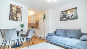 En moderne stue med en grå sofa, spisebord og stole, et køkken i baggrunden samt to billeder med motiver fra dyrelivet.
