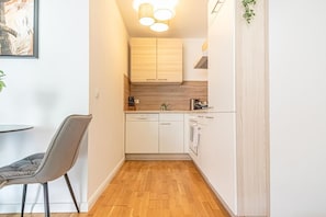 Une cuisine compacte avec des meubles blancs, un lave-vaisselle, une cuisinière et un coin repas équipé d’une chaise.