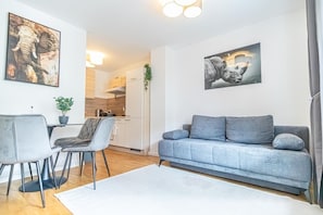 Un salon moderne avec un canapé gris, un coin repas avec des chaises, une cuisine en arrière-plan et des œuvres d’art accrochées aux murs.