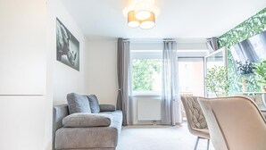 En moderne stue med en grå sofa, en lænestol, et stort vindue med gardiner og et billede hængt på væggen.