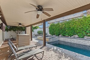 A covered patio area with a pool, outdoor seating, and a view of a cityscape.
