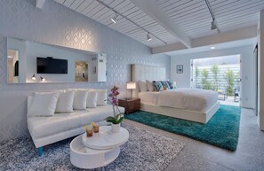 Ein modernes Schlafzimmer mit einem großen Bett, einer Couch, einem Fernseher und Blick ins Freie.
